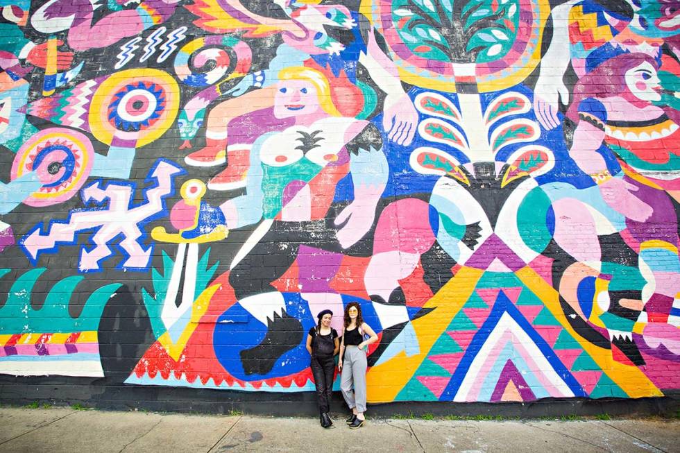 Two women standing in front an art wall