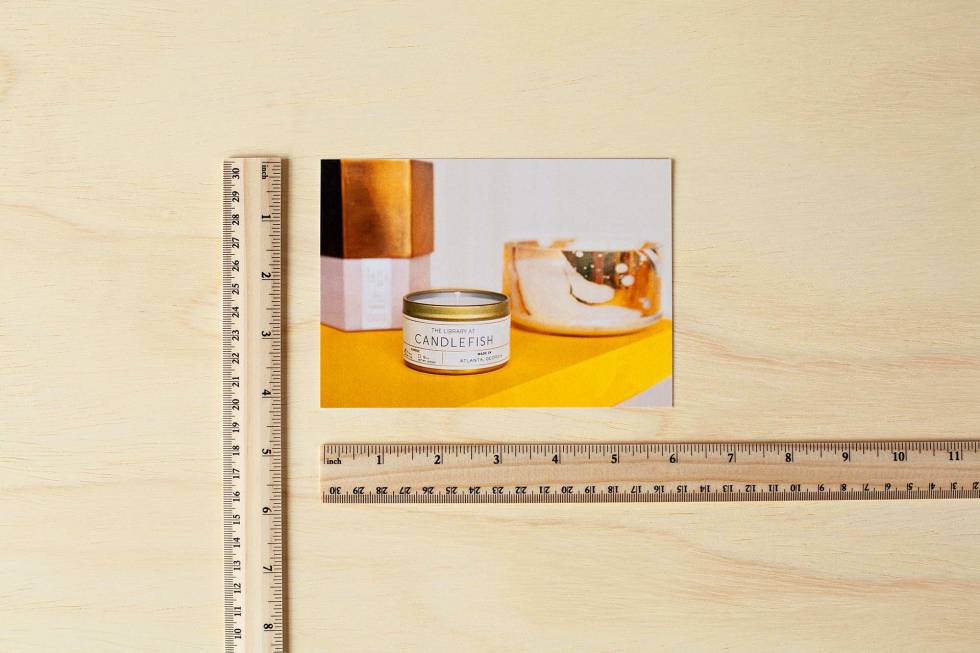 Photo of a postcard lined up against 2 rulers to show the dimensions
